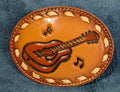 Brown leather belt buckle with guitar and music note design on a blue fabric background