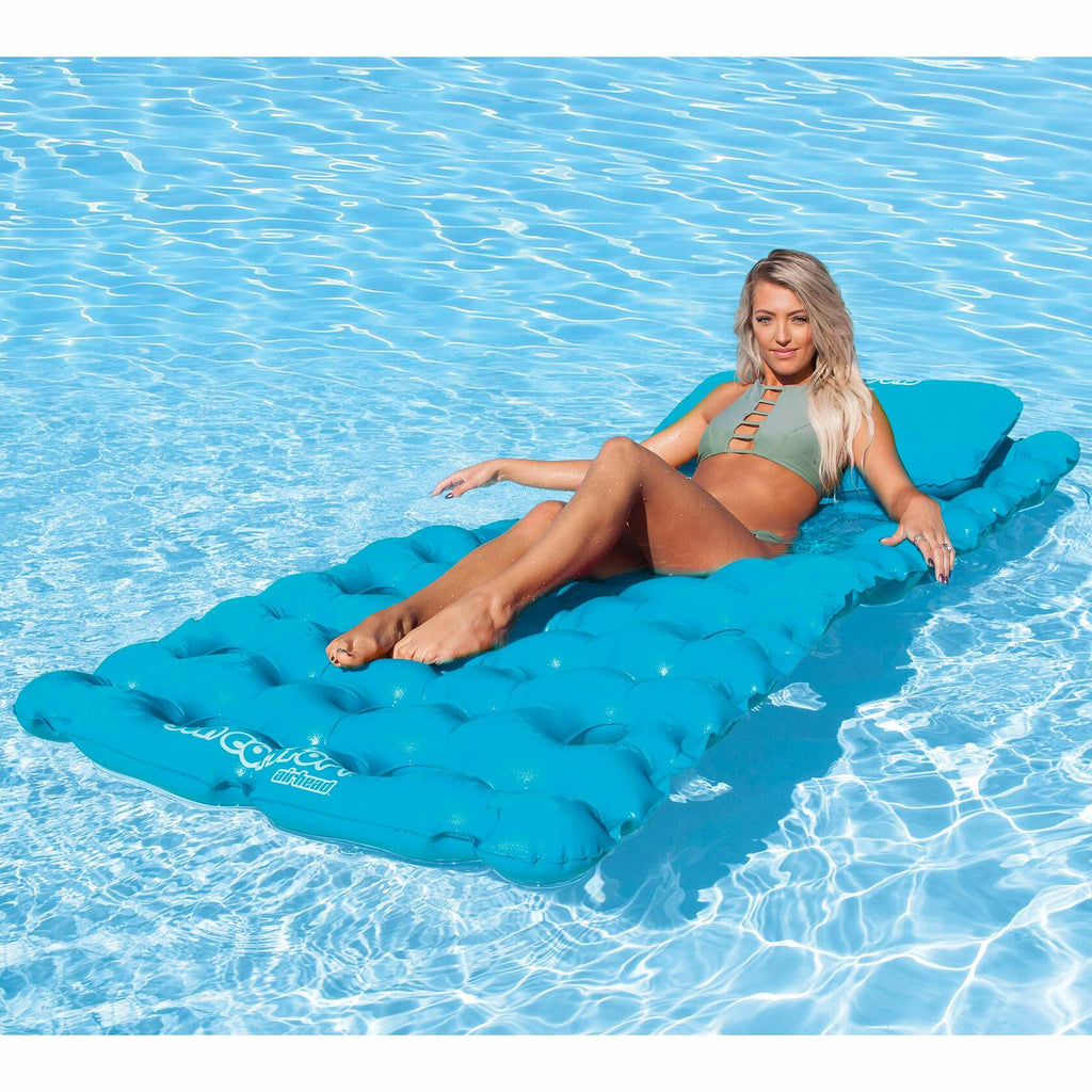 Woman lounging on a blue inflatable pool mat in clear blue water