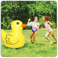 Two children playing with a large inflatable sprinkler duck toy in a grassy area.