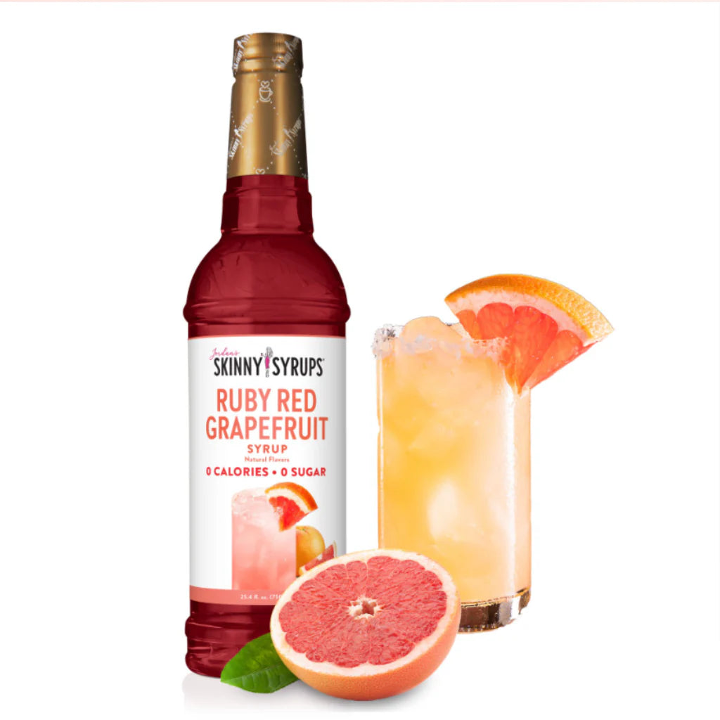 A bottle of Sugar Free Ruby Red Grapefruit Syrup from Jordan's Skinny Mixes, displayed alongside a glass with ice and grapefruit slices, and a half grapefruit in front.