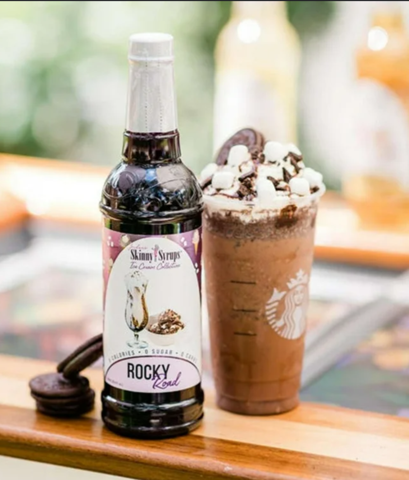 Bottle of Skinny Syrups Rocky Road syrup next to a Starbucks drink with whipped cream and cookies.