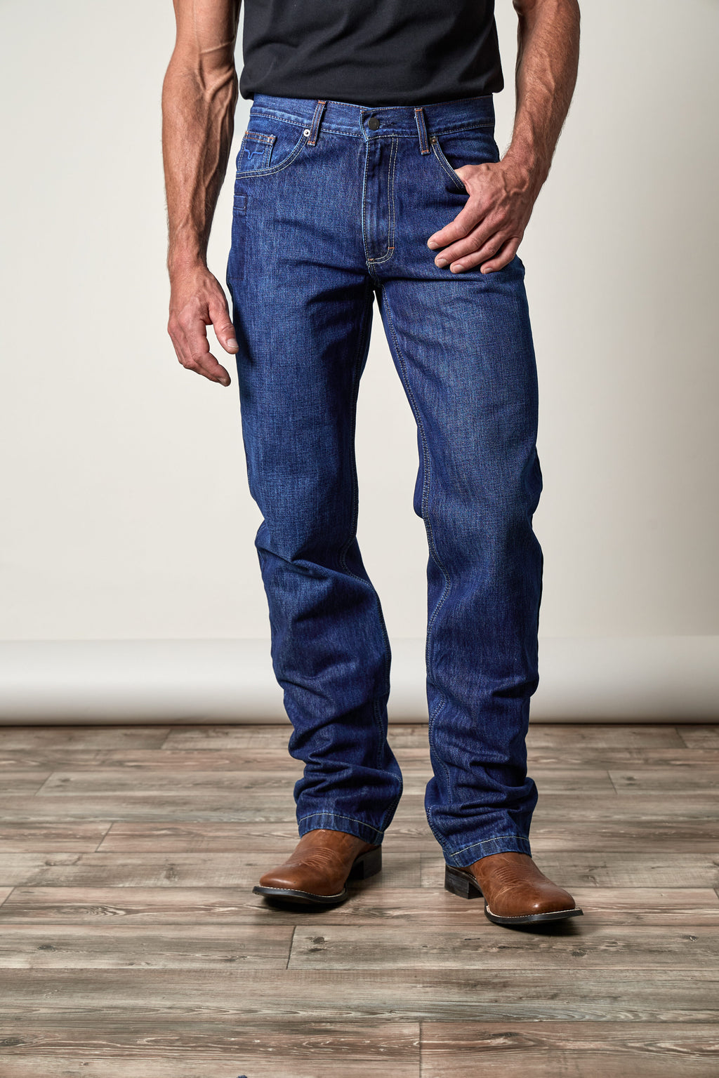 Model wearing Kimes Ranch Dillon men's dark wash relaxed bootcut western jeans with brown leather cowboy boots.