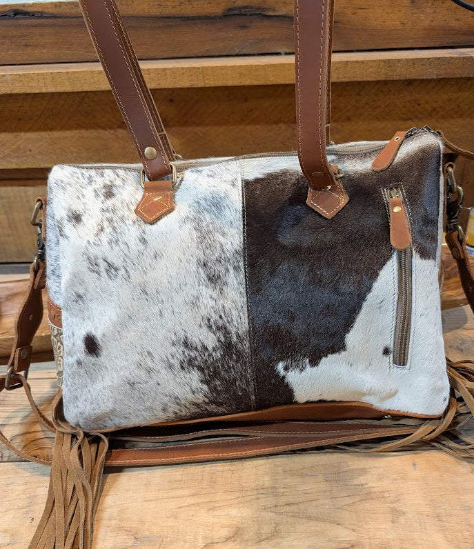 Cowhide leather handbag with brown leather straps on a wooden surface