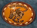 Leather belt buckle with donkey design and 'High Country Pick Up' text on a blue textured background