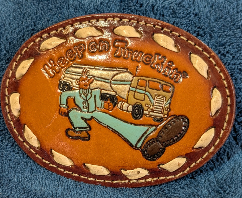 Leather belt buckle with 'Keep on Truckin'' design on a blue fabric background