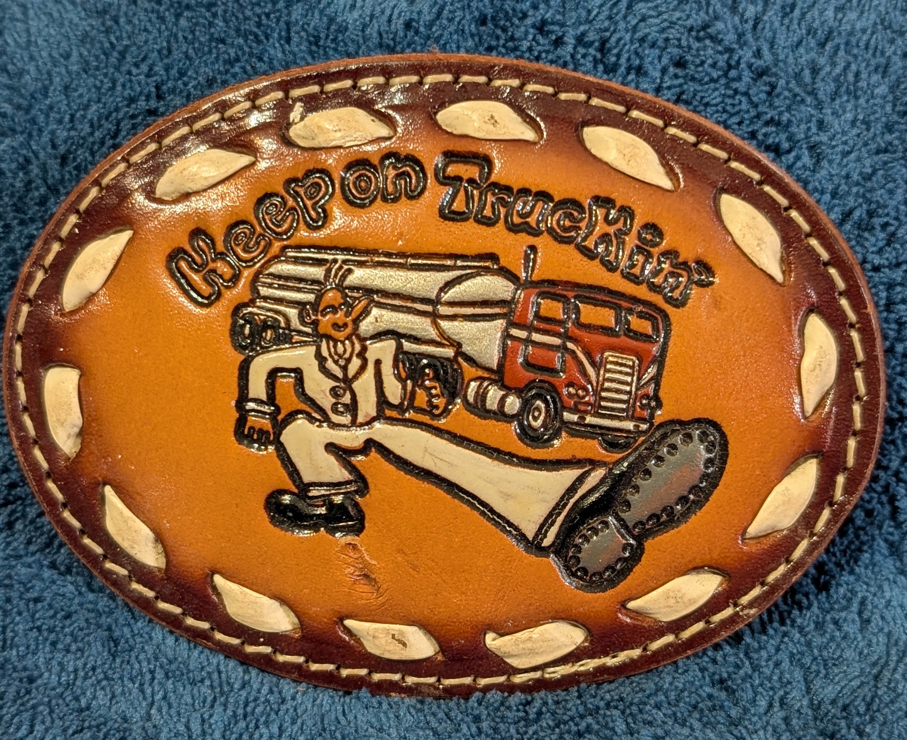 Leather belt buckle with truck design and 'Keep on Truckin'' text on a blue textured background