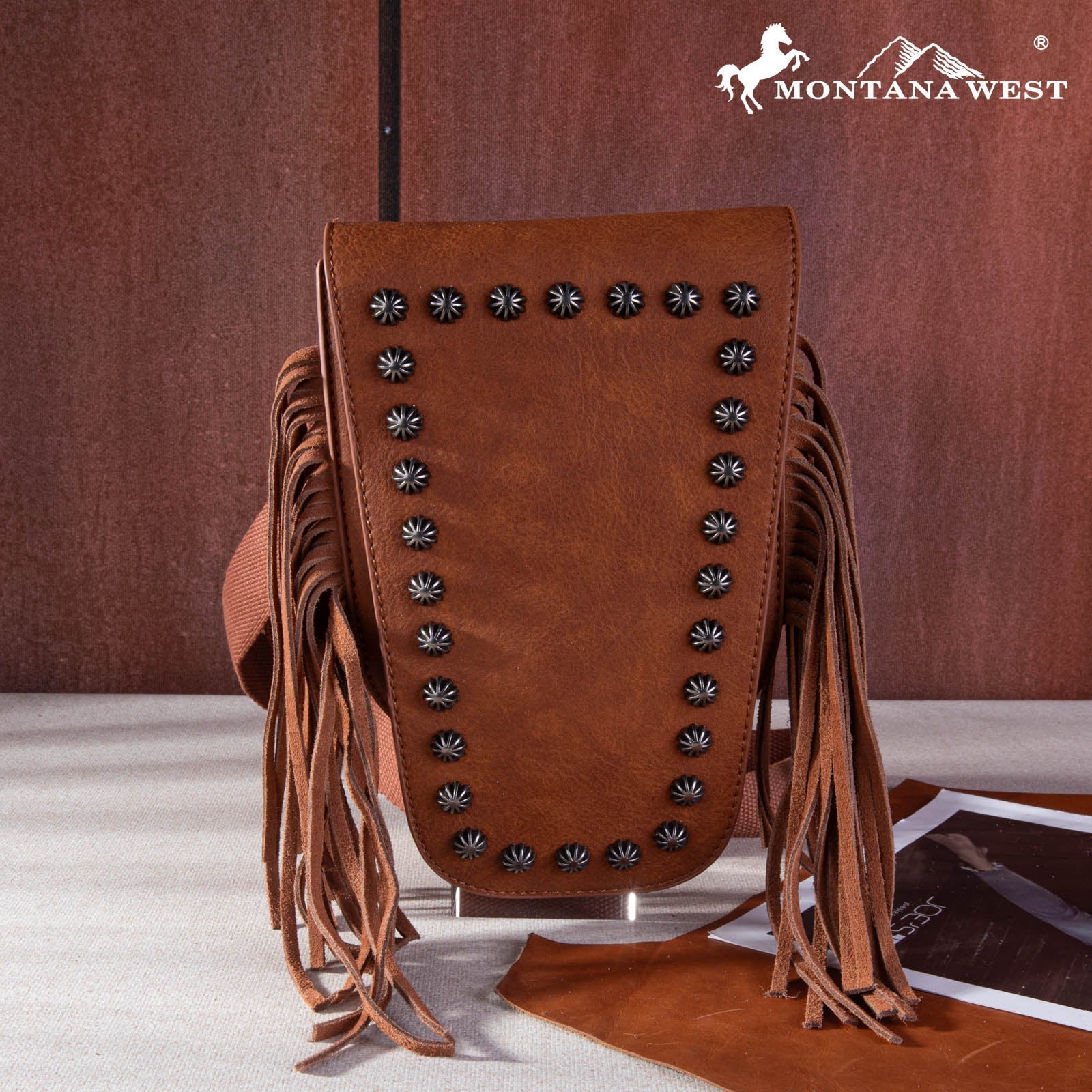 Brown leather bag with fringes and studs on a brown background, featuring the Montana West logo.