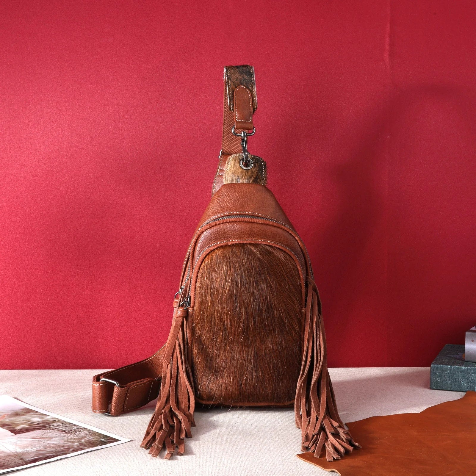 Brown leather sling bag with fringes on a red background