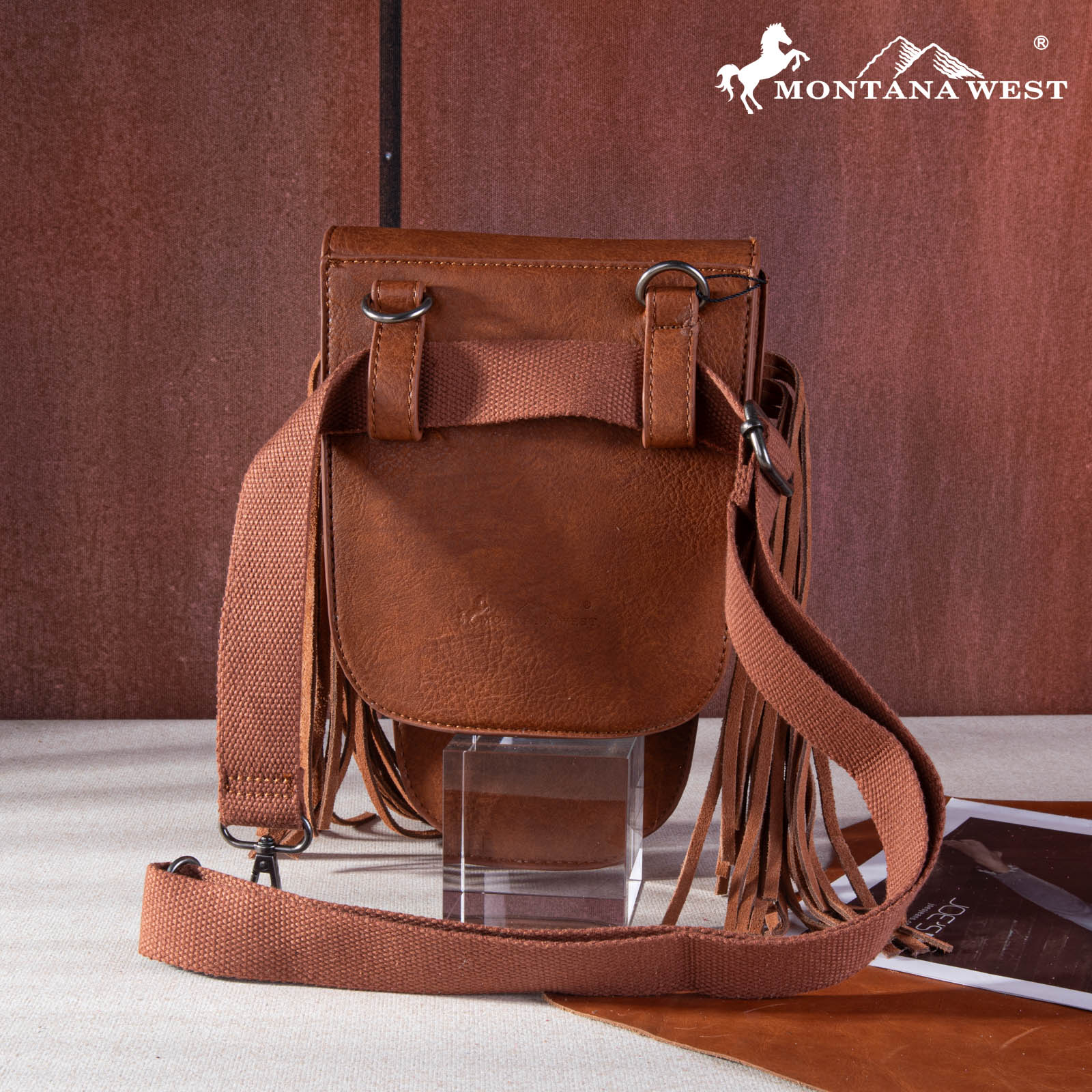 Brown leather bag with fringes on a brown background, featuring the Montana West logo.