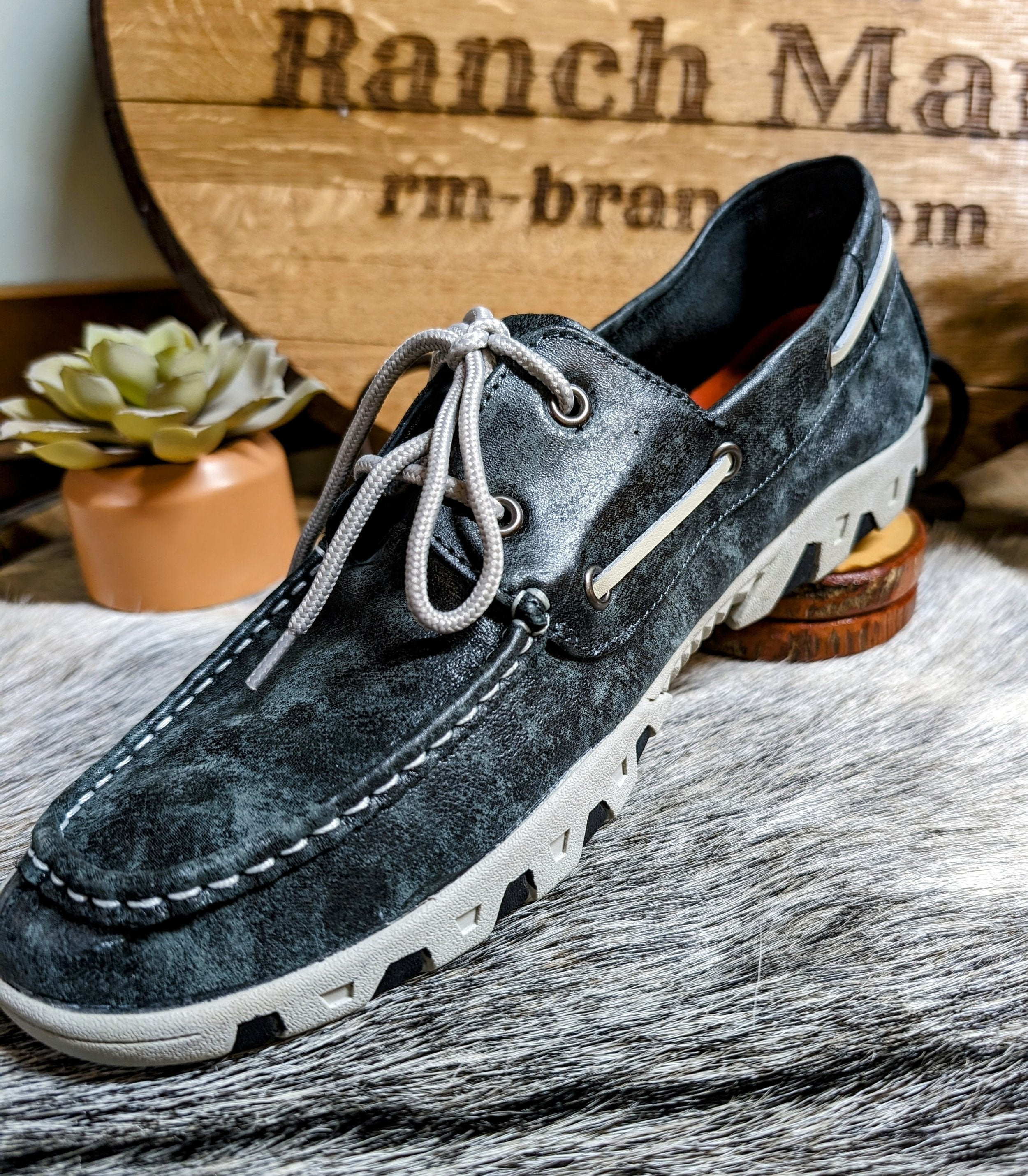 A Ferrini men's leather loafer in smokey black color, displayed against a rustic background with a wooden sign.