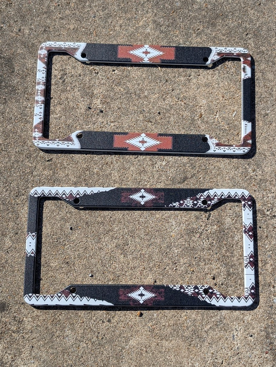 Two decorative license plate frames with aztec  patterns on a concrete surface.