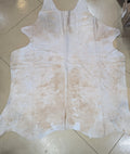 A splotchy champagne-colored cowhide rug laid out on a floor.