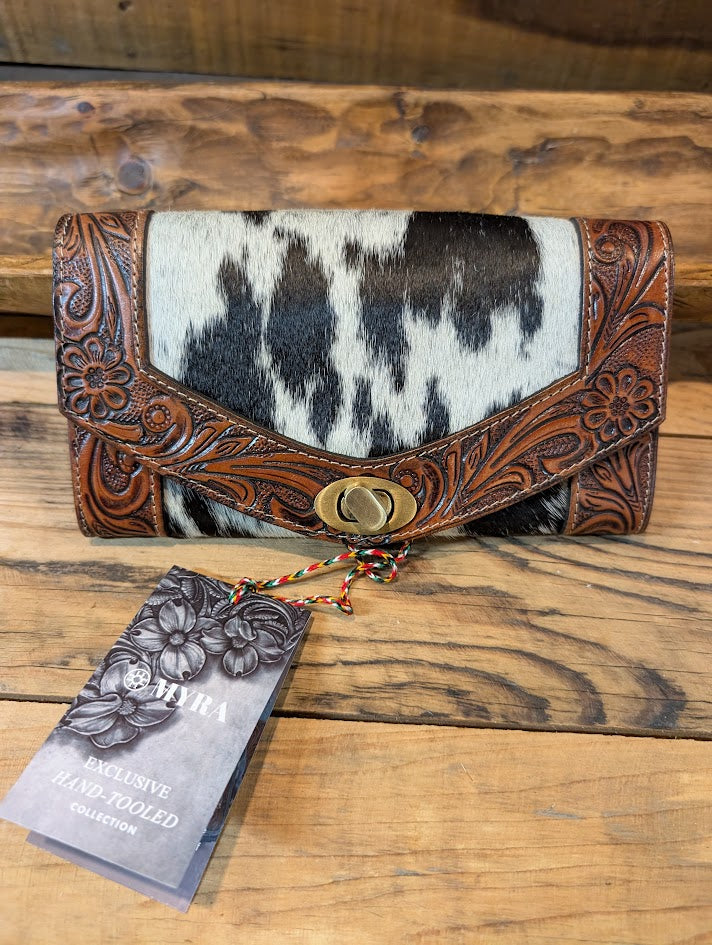 Handcrafted leather wallet with cowhide pattern on a wooden surface, featuring a tag from 'Myra'.