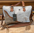 Cowhide leather bag with brown leather straps on a wooden surface