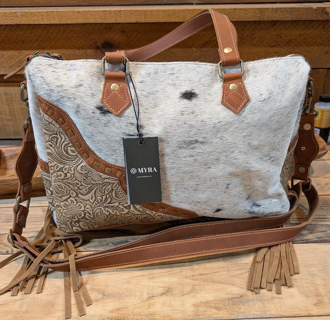Cowhide leather bag with brown leather straps on a wooden surface