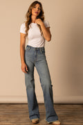 Woman wearing a white t-shirt and blue Kime ranch Olivia jeans standing against a beige wall.