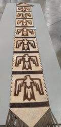 An 8ft cowhide table runner featuring a distinctive thunderbird design with brown patterns on a white background.