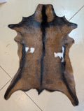A genuine goat hide with a brown, black, and white color pattern laid out on a floor.