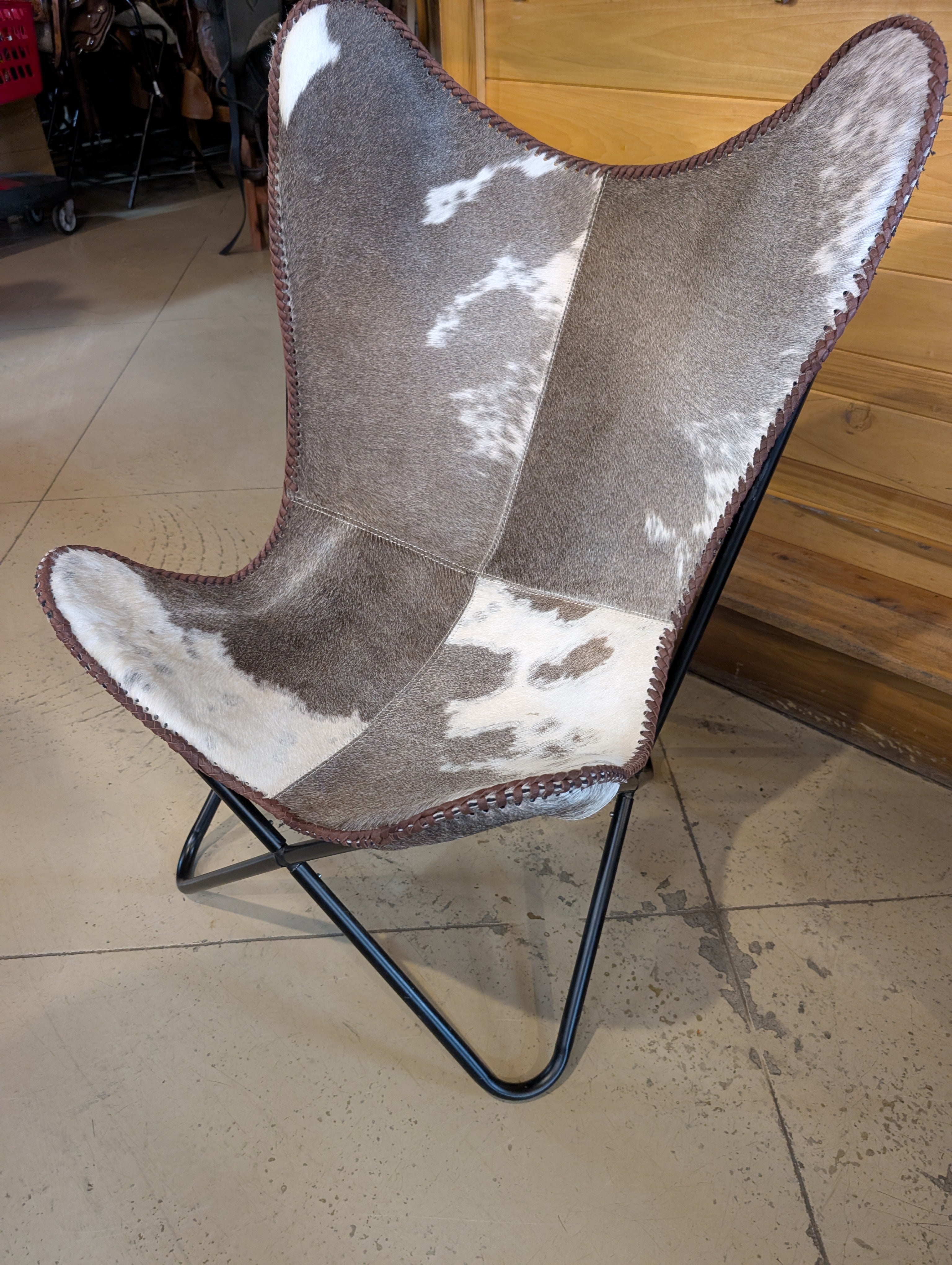 Genuine cowhide accent chair with natural brown and white hide upholstery, shown assembled in rustic living room.