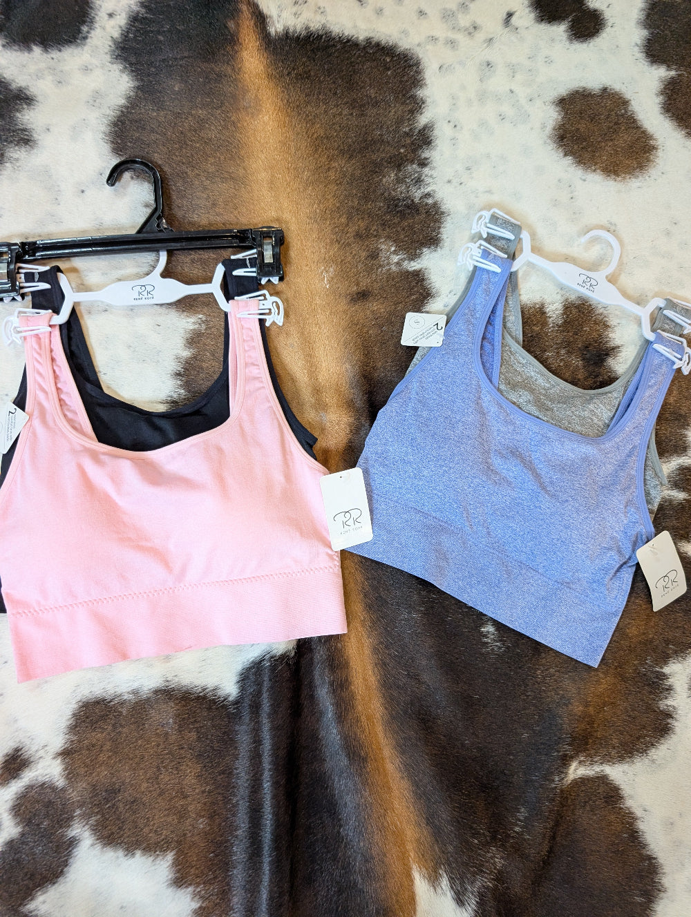 Two sports bras on hangers with tags against a cowhide rug background