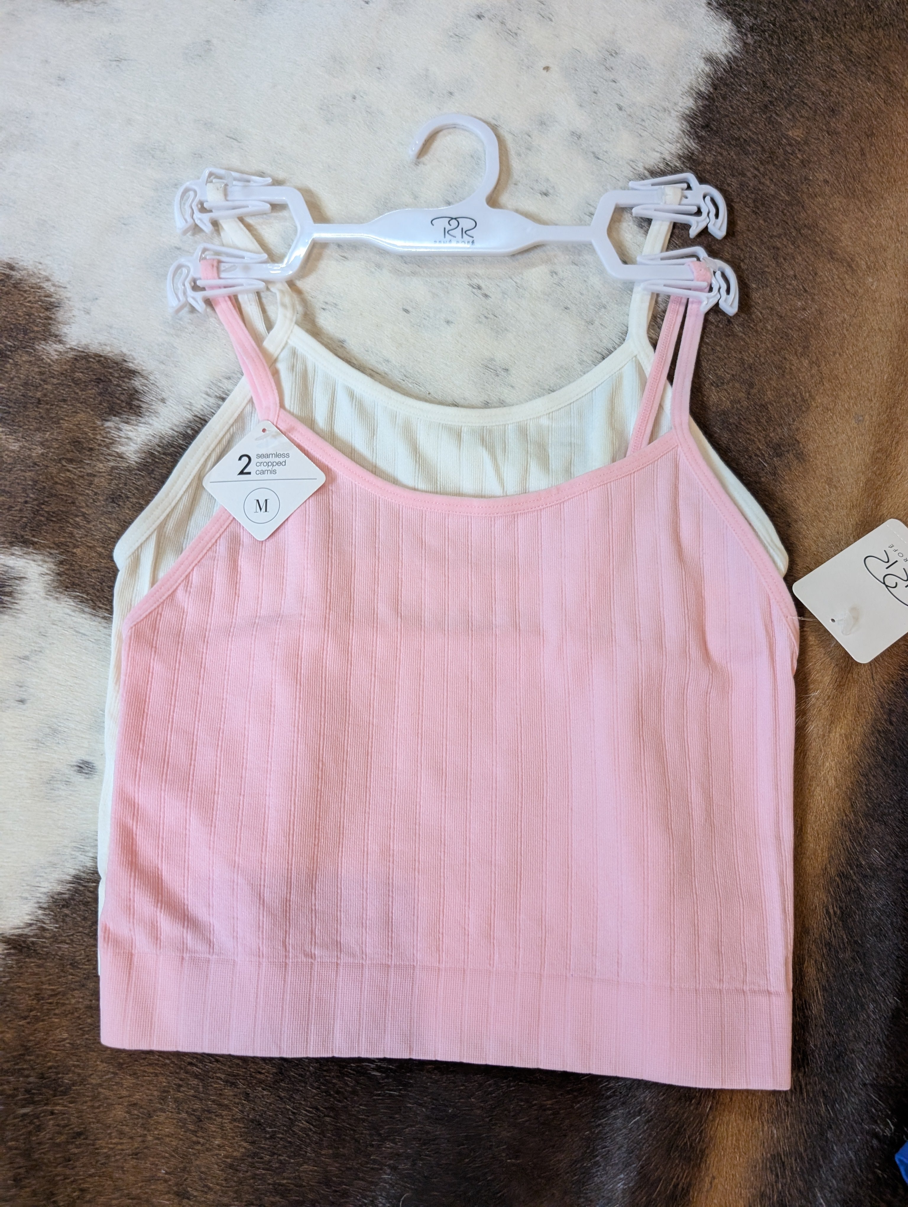 Pink ribbed tank top on a hanger with a white label against a brown and white patterned background