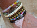 Stack of colorful beaded bracelets with tassels on a wrist against a neutral background