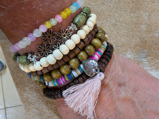 Stack of colorful beaded bracelets with tassels on a wrist against a neutral background
