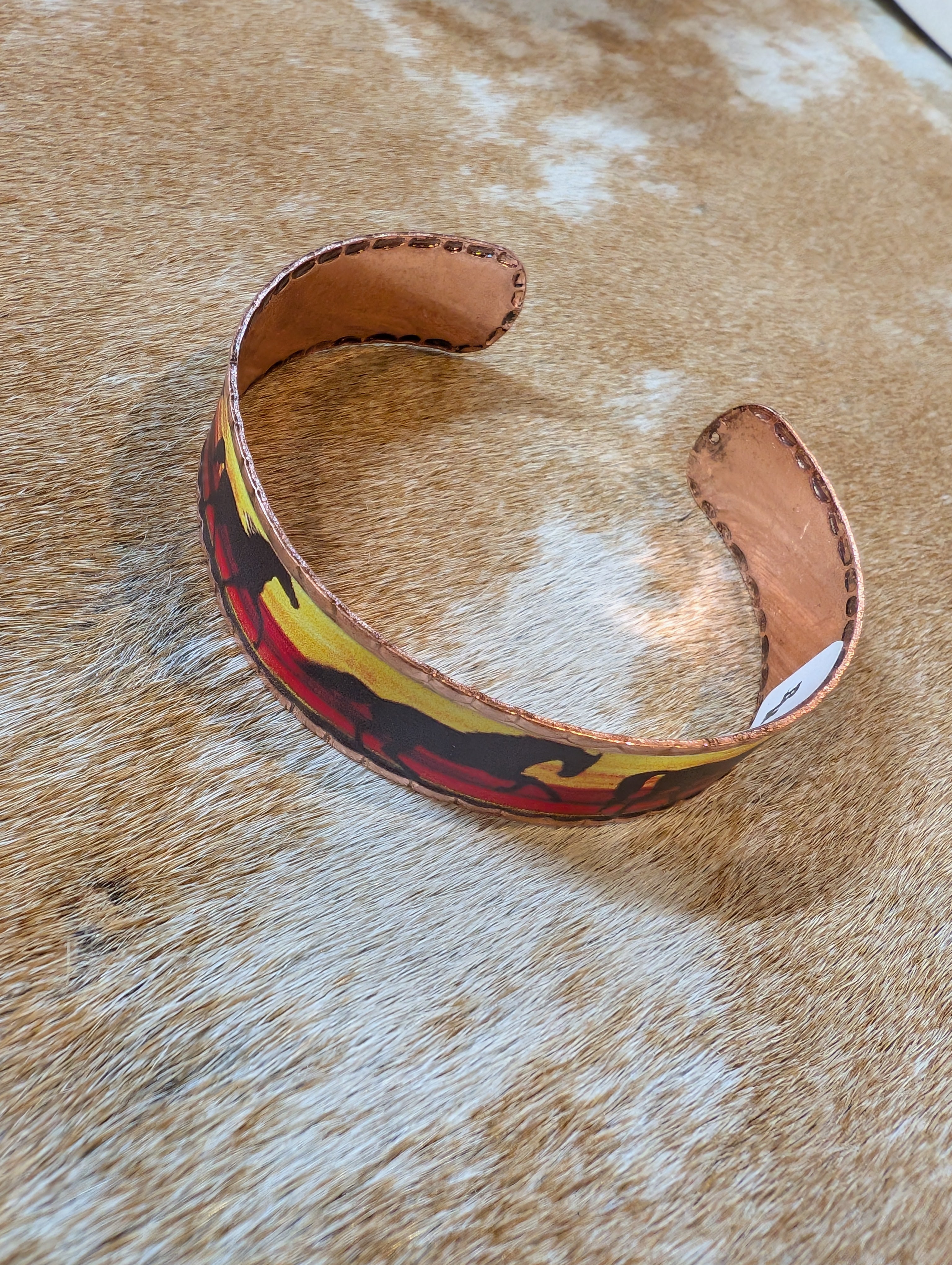 Copper-tone cuff bracelet with etched running horse design shown on cowhide rug