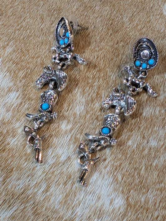 Western Trails jewelry collection featuring fashion pendants and earrings shaped like boots, hats, horses, and guns displayed on rustic background