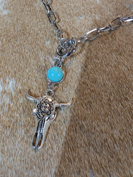 Necklace with a silver bull head pendant and turquoise stone on a brown leather background