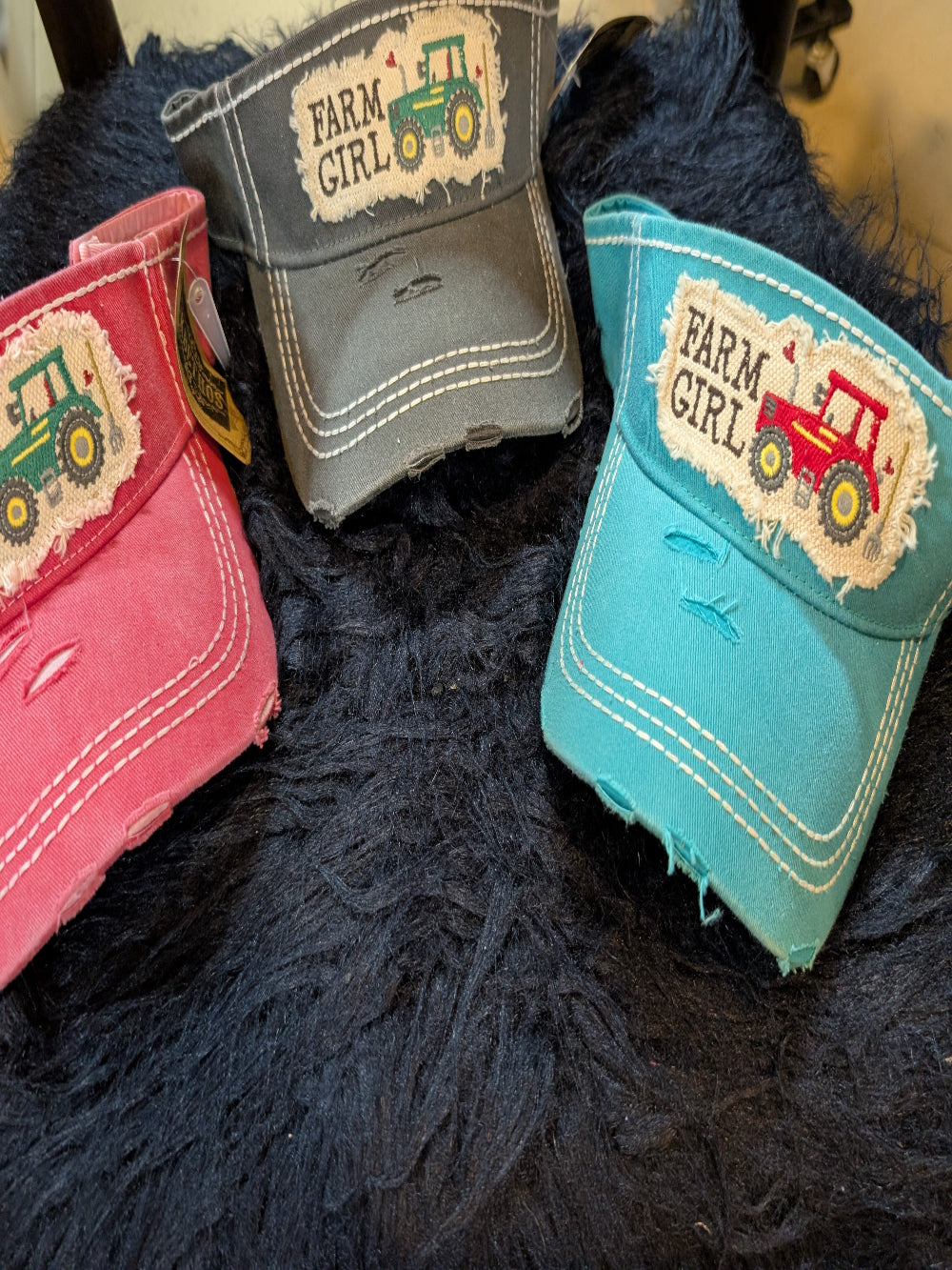 Three colorful caps with 'Farm Girl' and tractor designs on a dark textured surface.