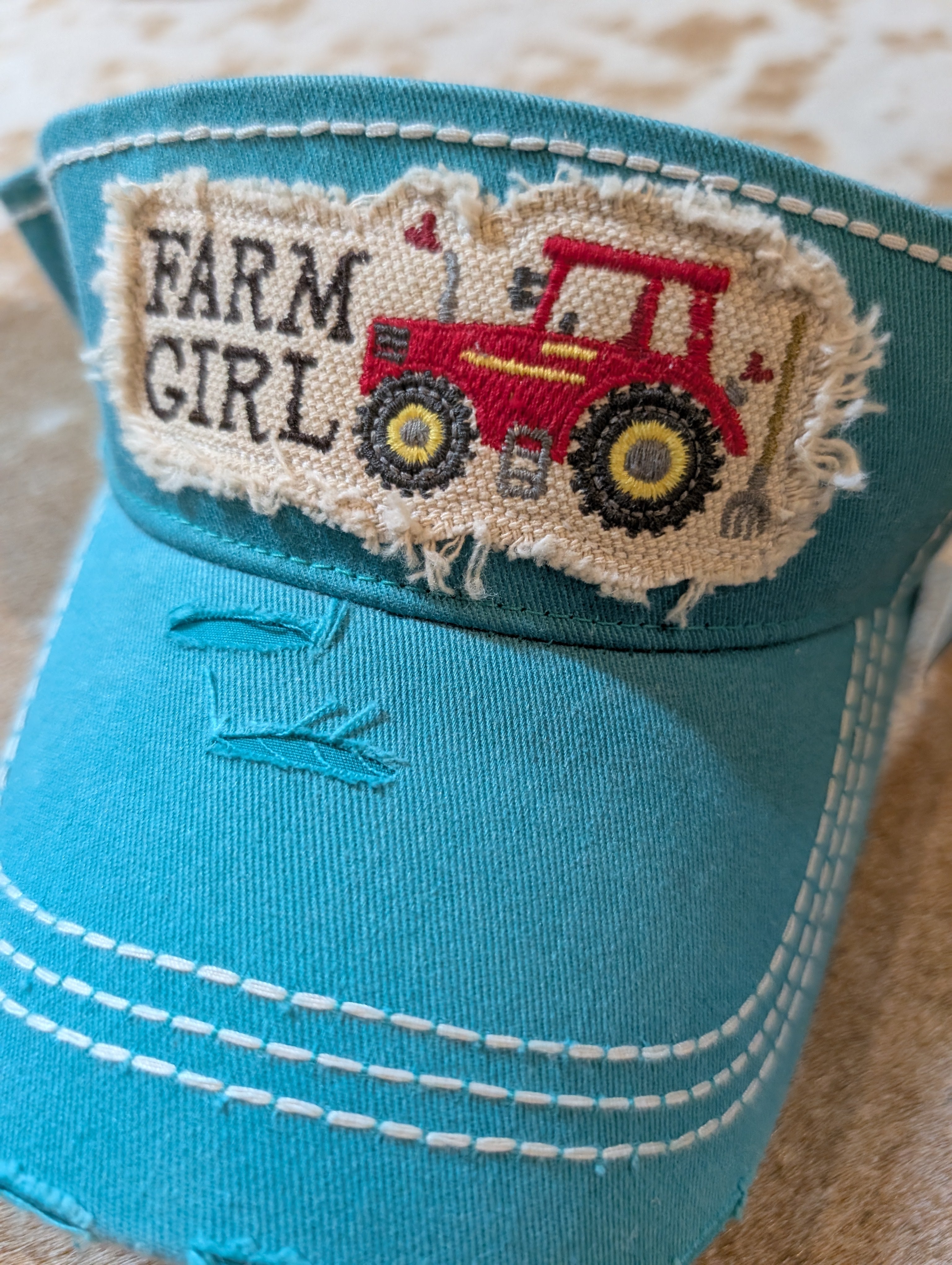 Distressed Farm Girl visor in rustic color with embroidered front shown on cowhide background
