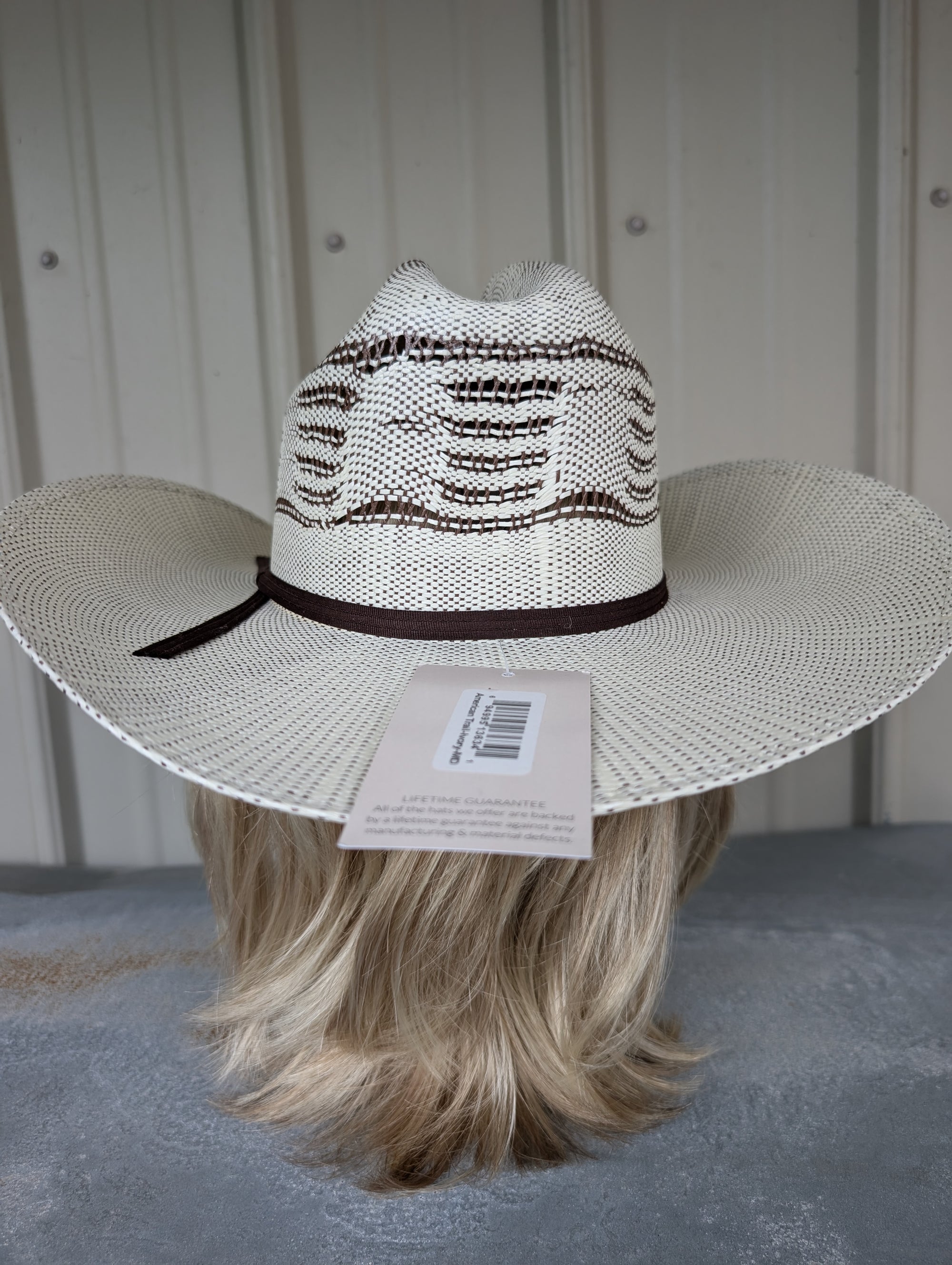 White cowboy hat with brown band on a mannequin head against a white wall.