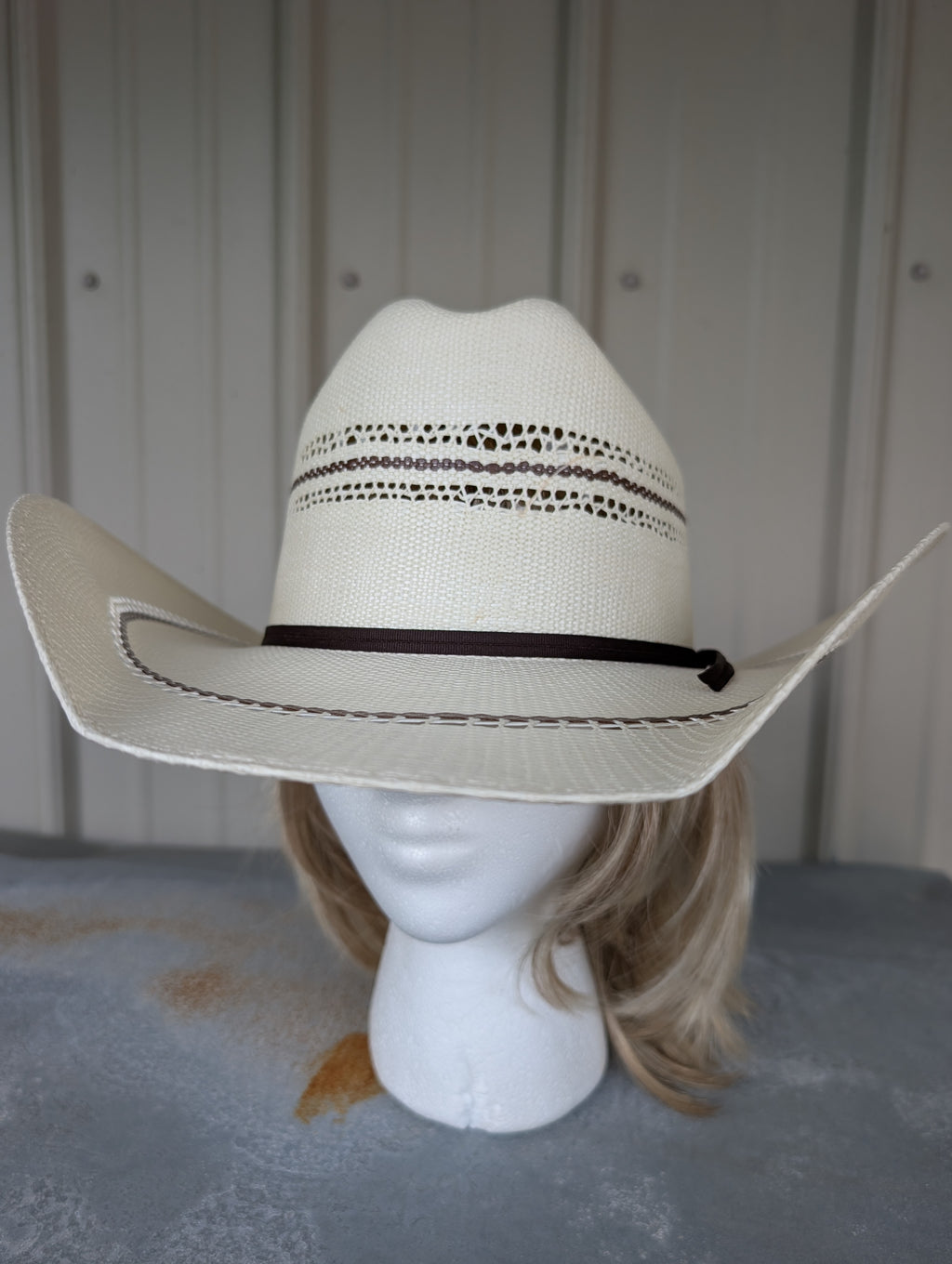 White cowboy hat with brown band on a mannequin head against a neutral background