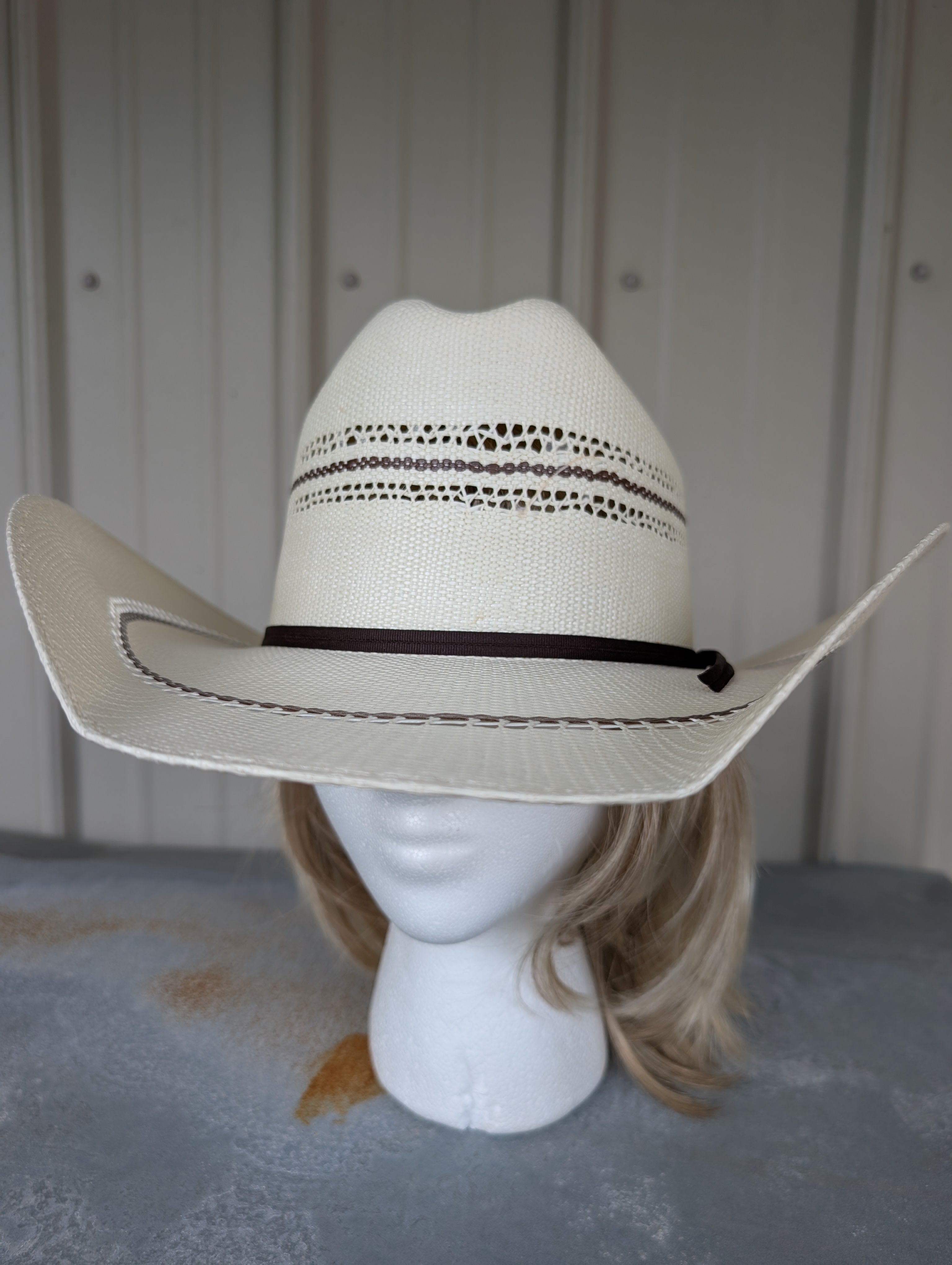 White cowboy hat with brown band on a mannequin head against a neutral background