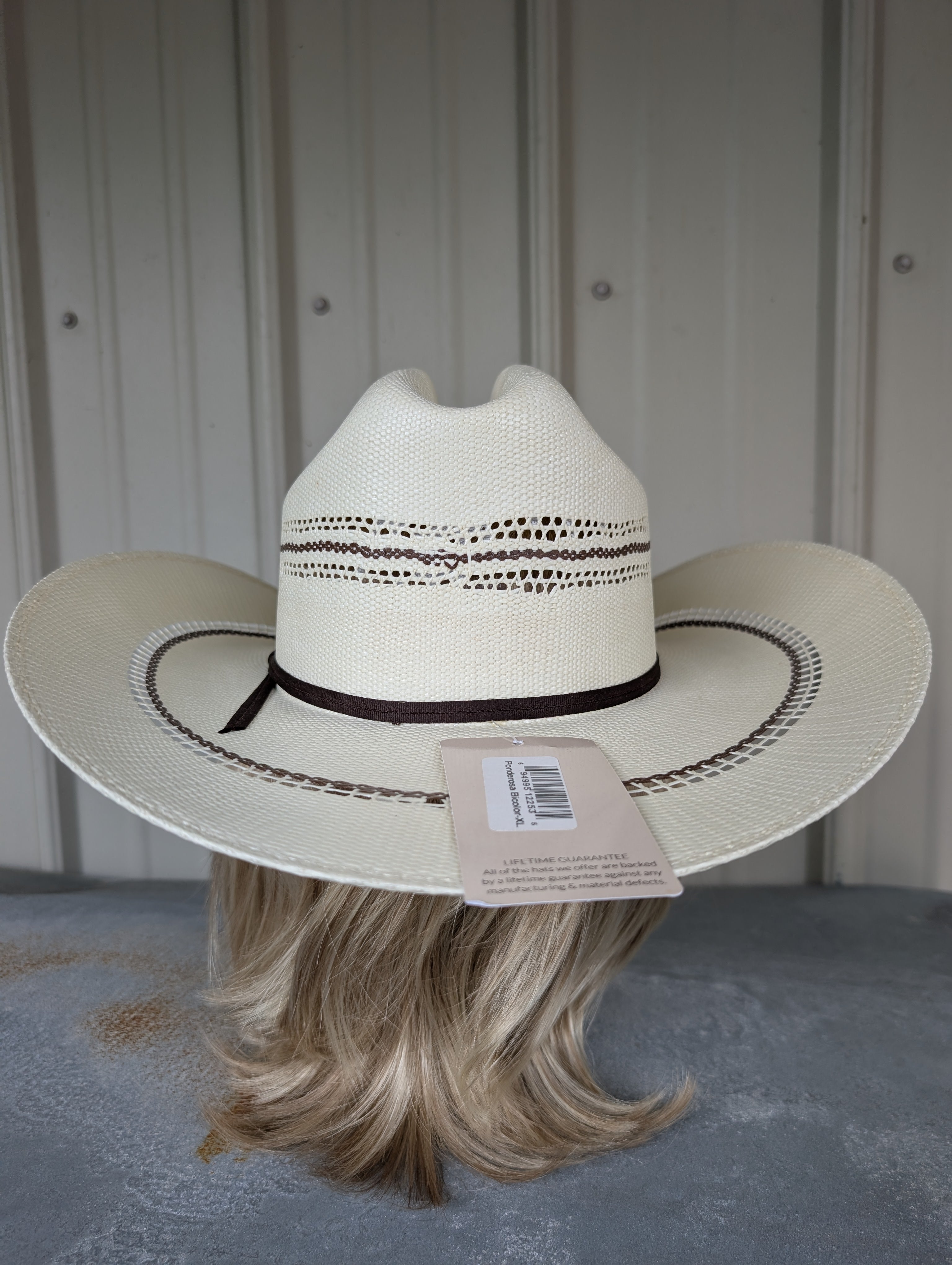 White cowboy hat with a black band on a mannequin head against a gray background