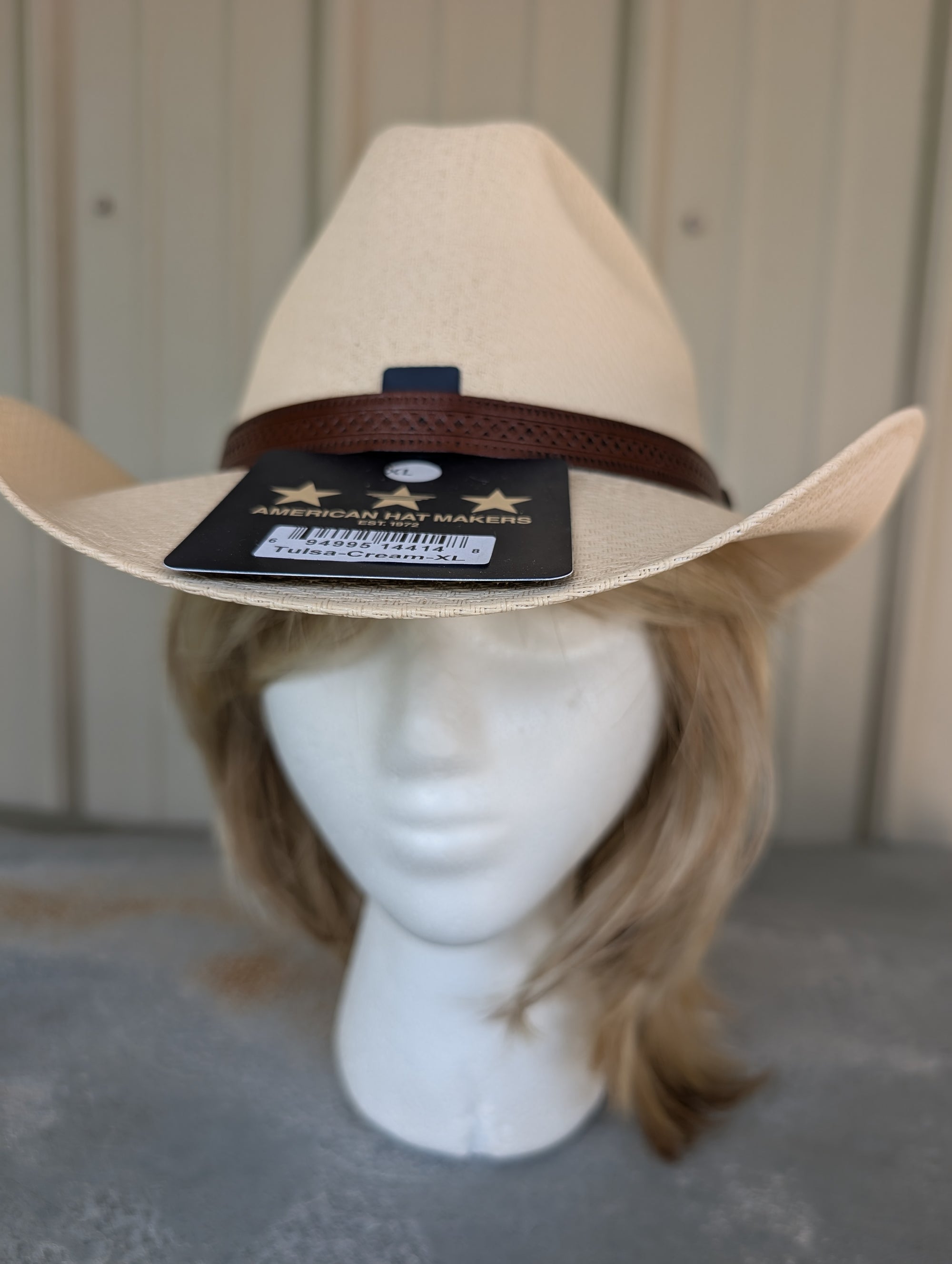 Beige cowboy hat on a mannequin head with a visible brand tag against a neutral background