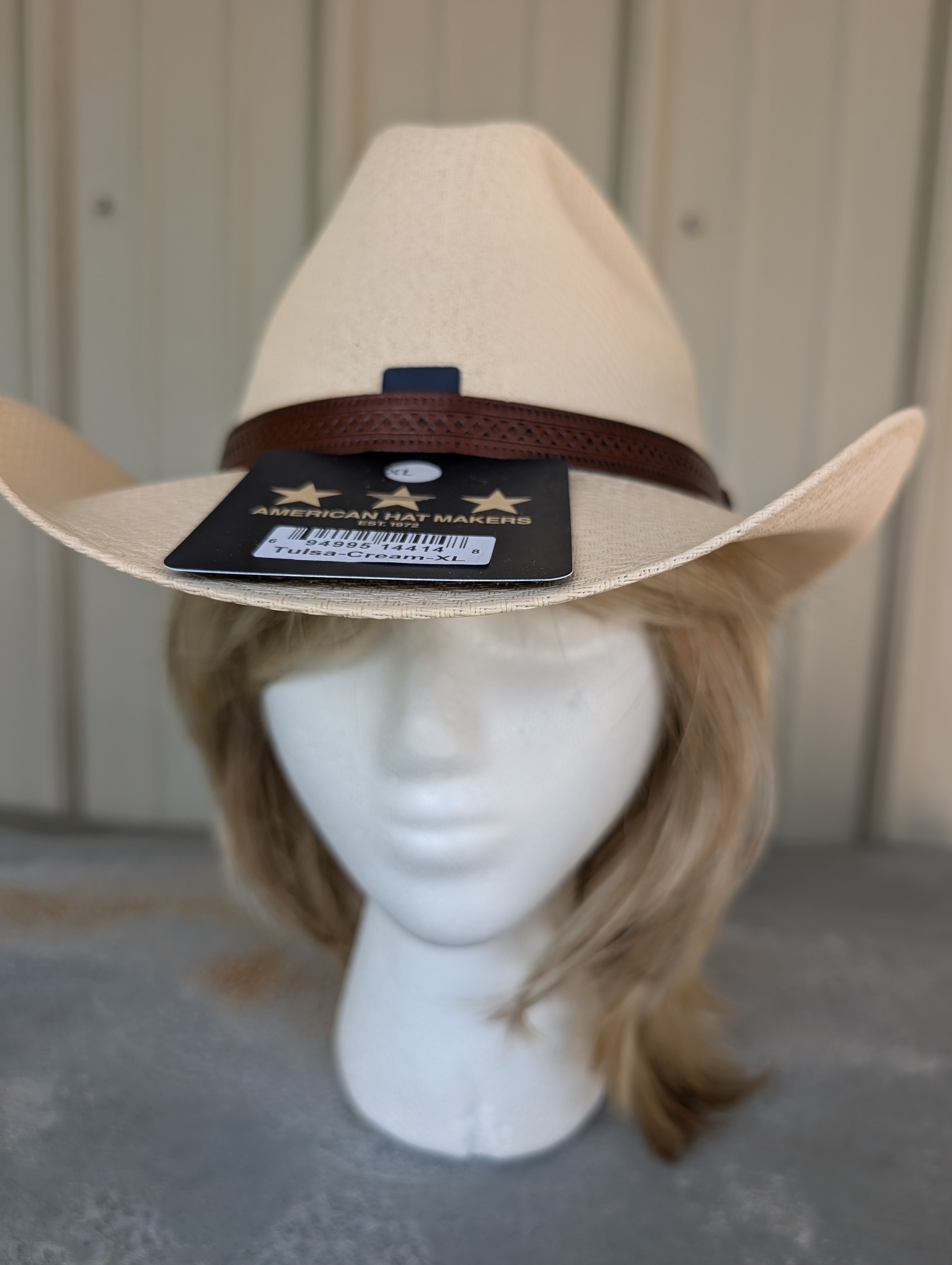 Beige cowboy hat on a mannequin head with a visible brand tag against a neutral background