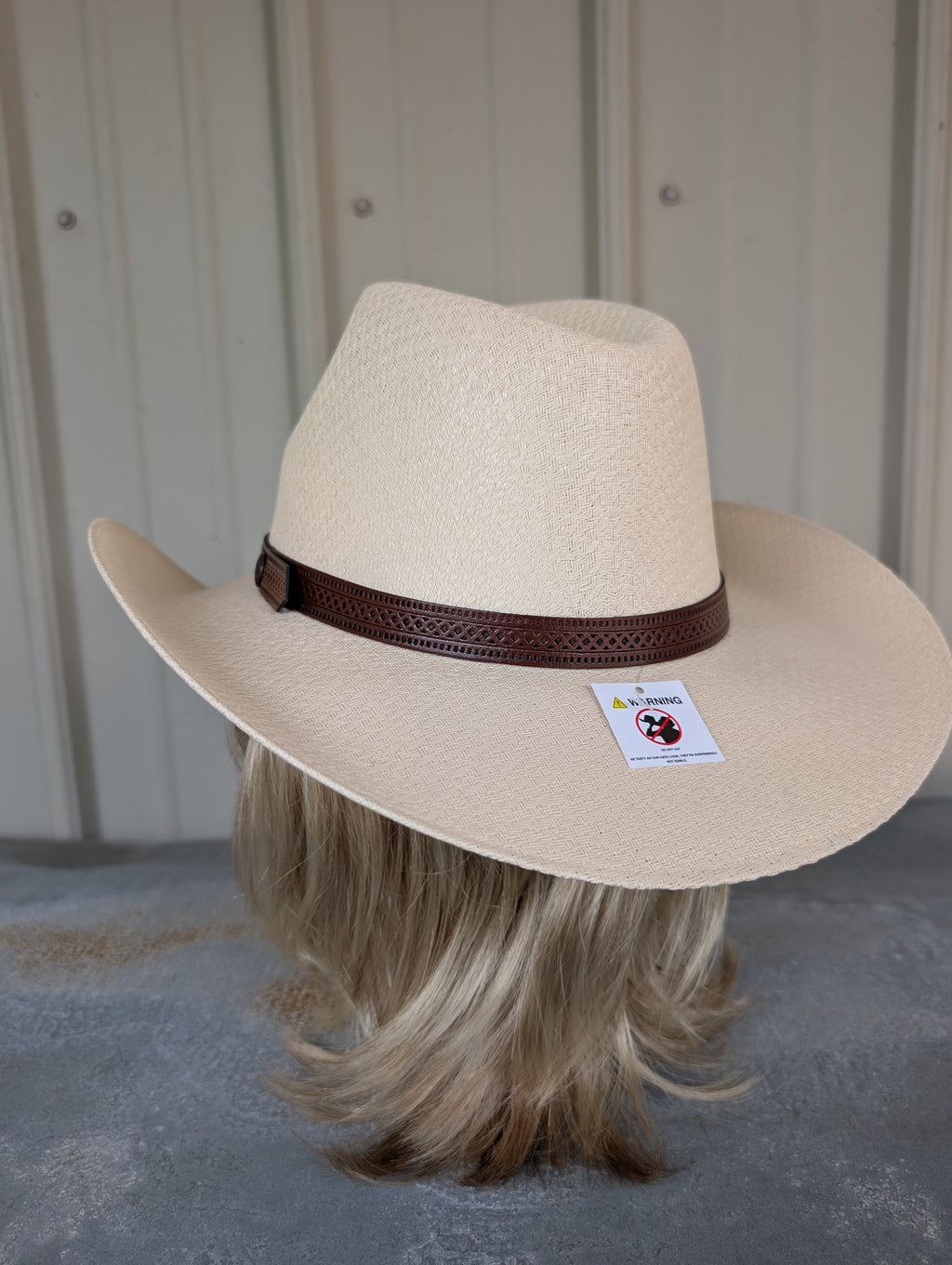 Beige cowboy hat with a brown band on a mannequin head against a neutral background