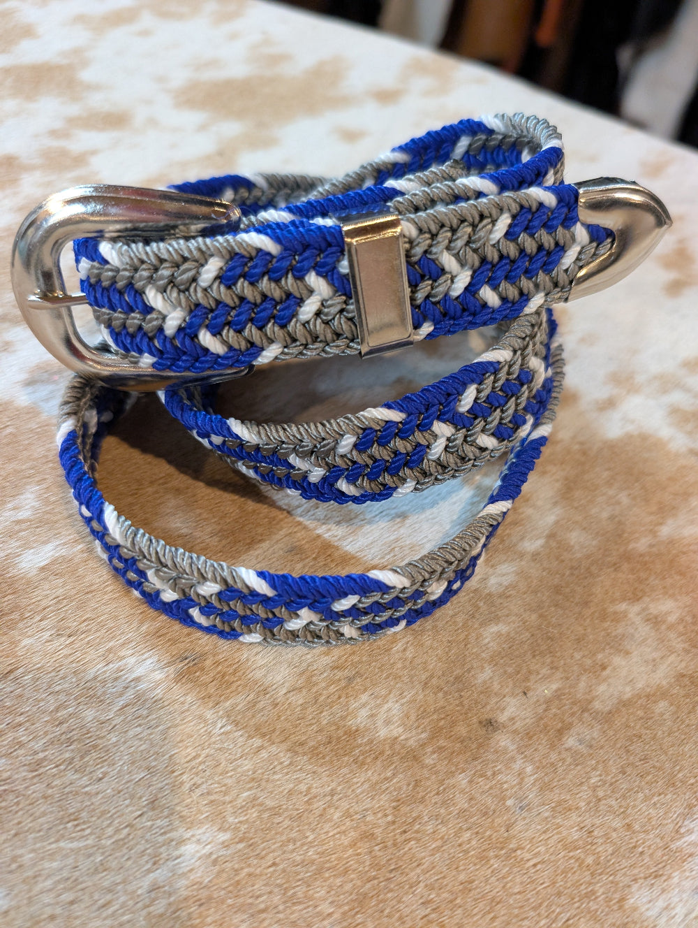 Blue, gray, and white braided belt with a silver buckle on a textured surface.