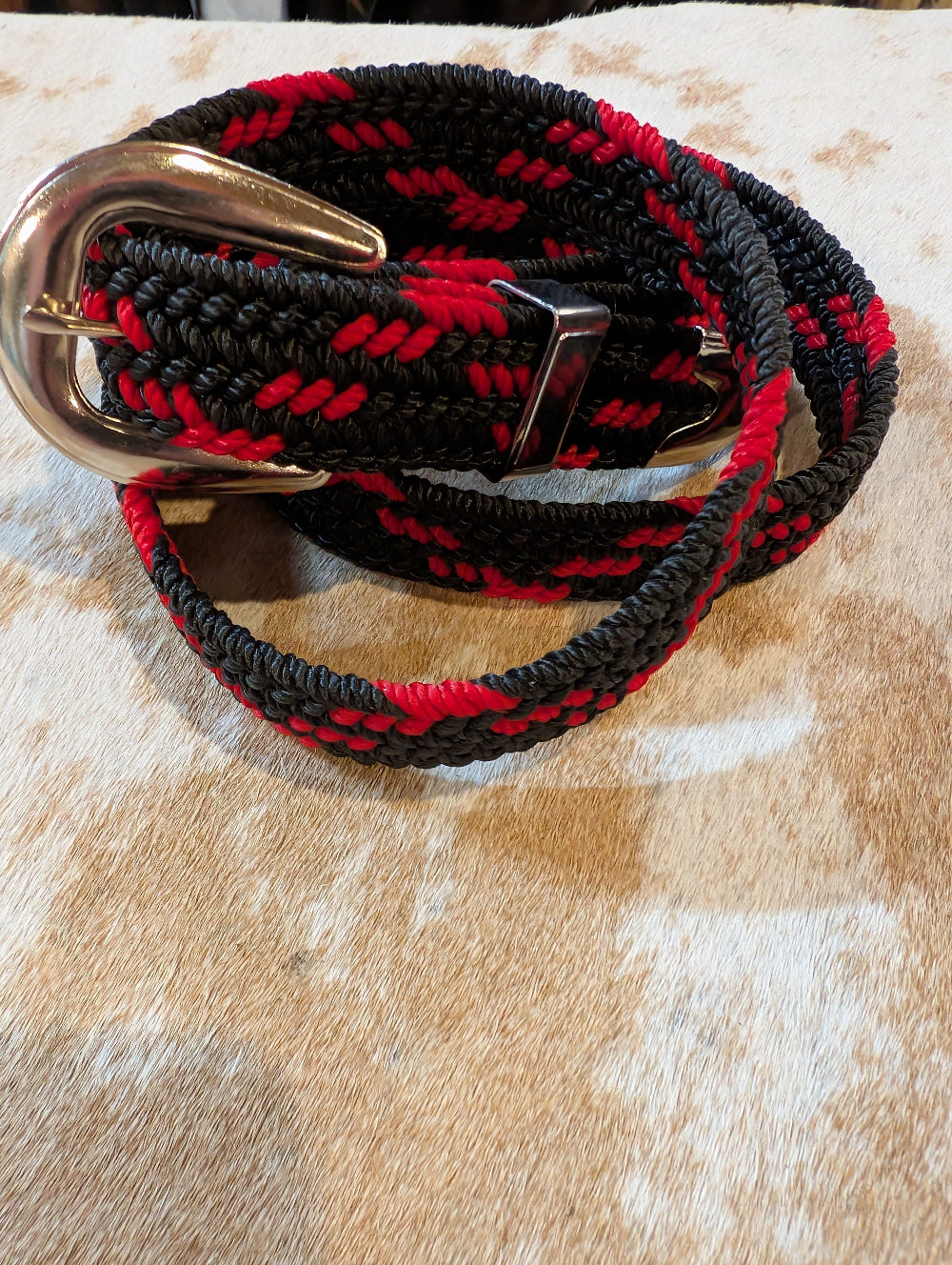 Black and red braided belt with a gold buckle on a textured surface