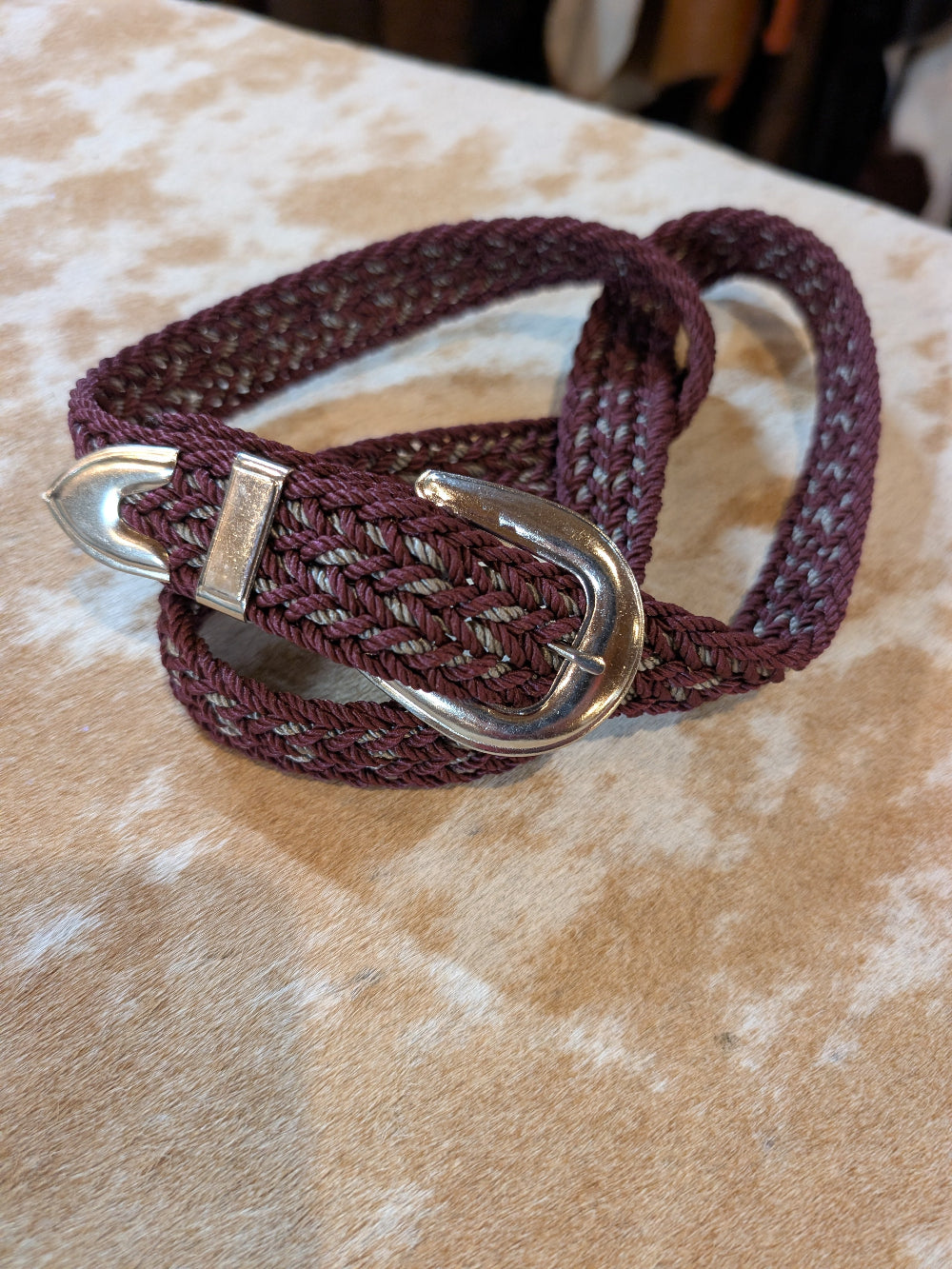 Maroon braided belt with silver buckle on a textured surface