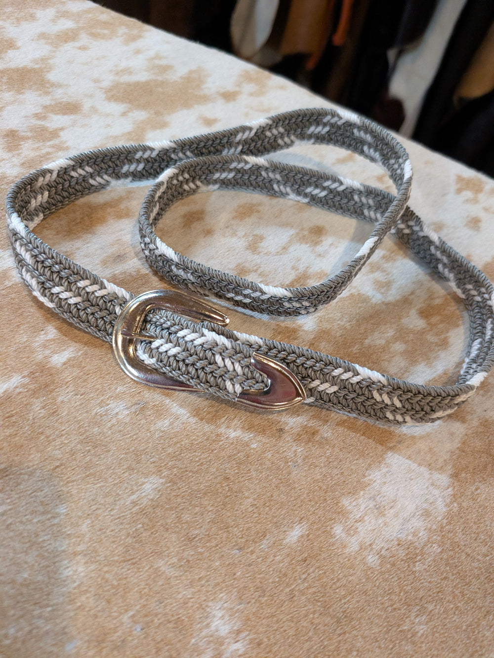 Gray braided belt with a metal clip on a textured surface