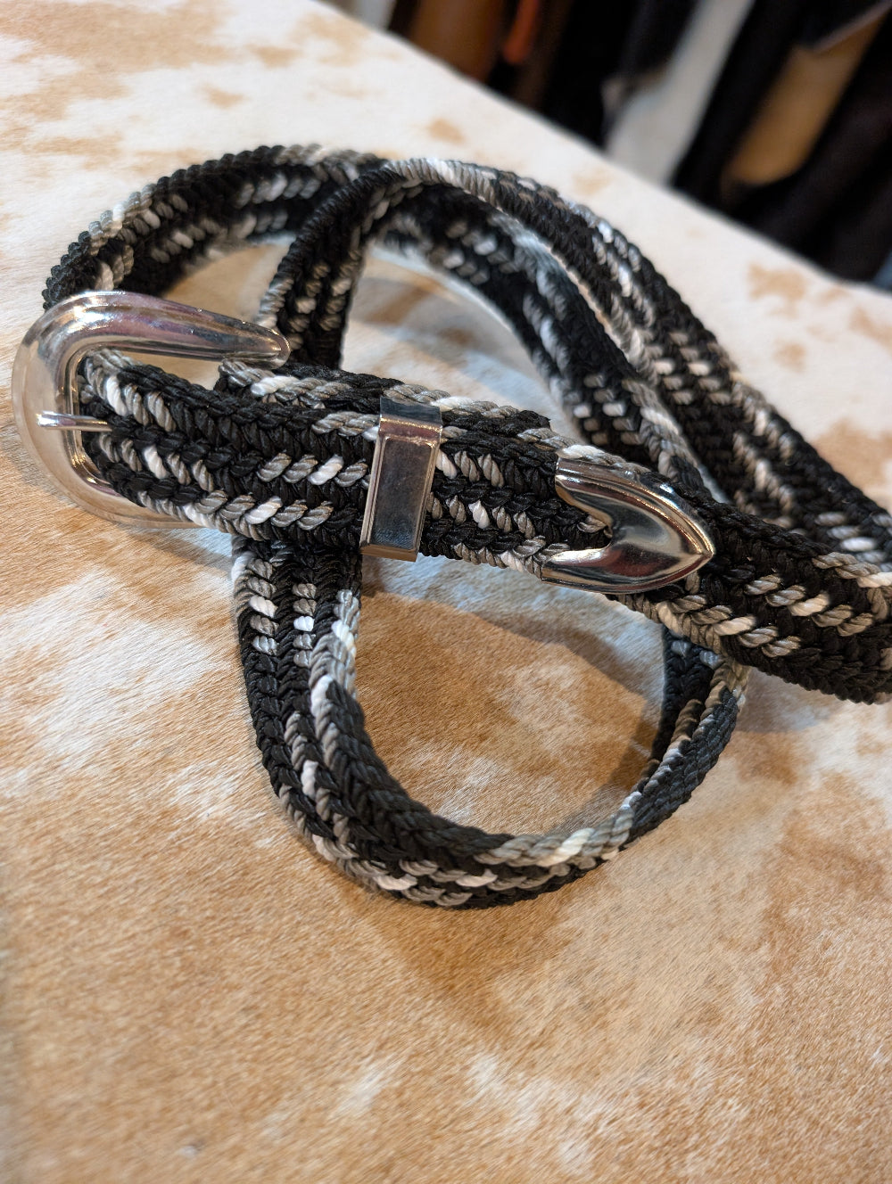 Black and white braided belt with metal clips on a beige surface