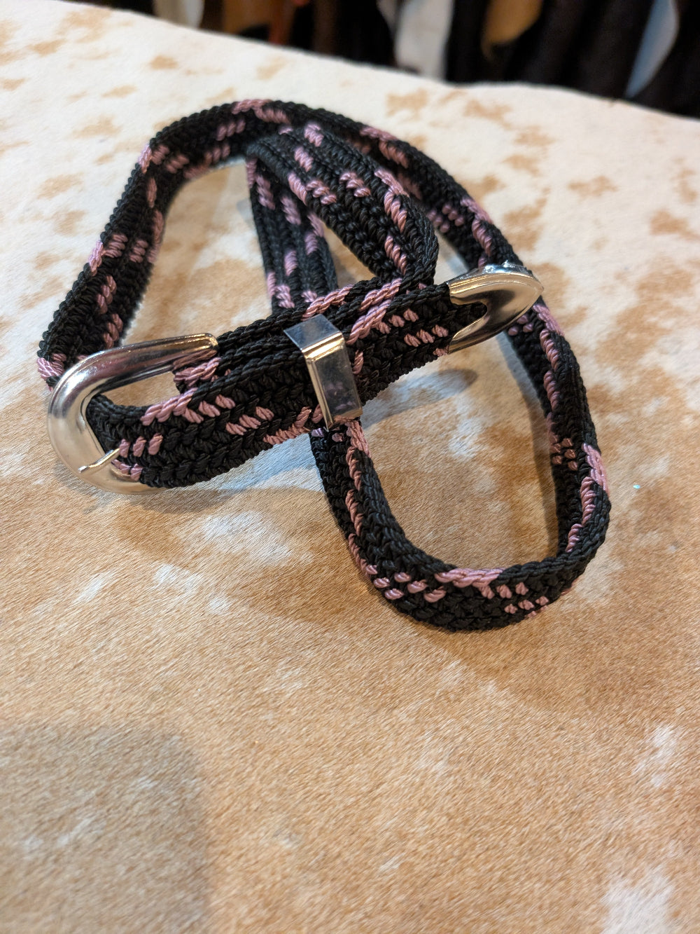 Black and pink braided belt with a metal clip on a beige surface 