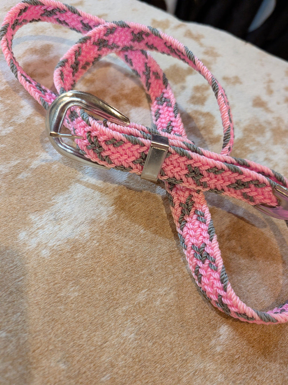 Pink and gray braided belt with a metal clip on a brown leather surface.