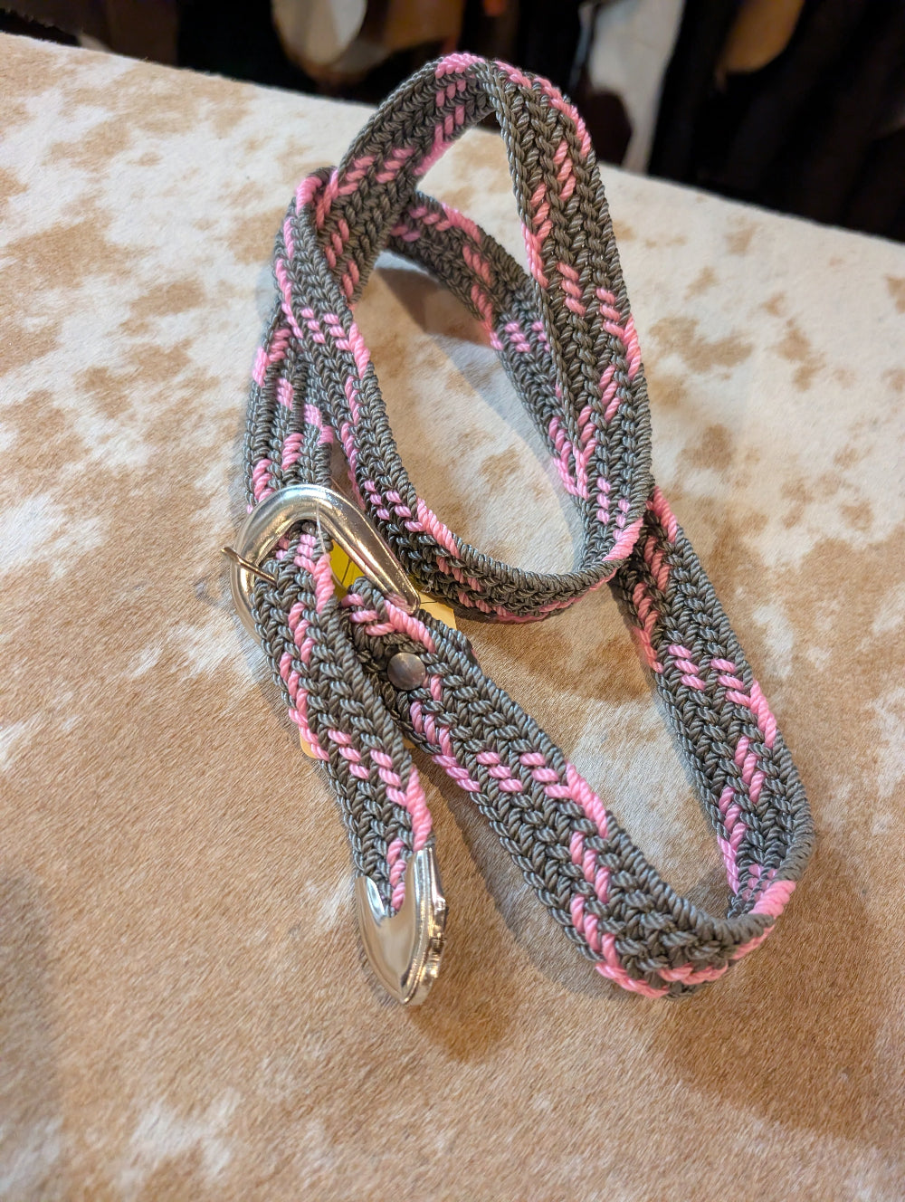 Gray and pink braided belt with a metal clip on a textured surface
