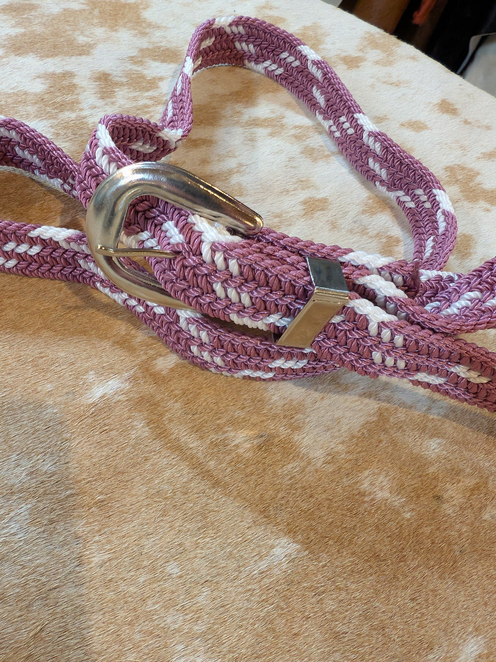 Purple and white braided belt with a gold buckle on a textured surface