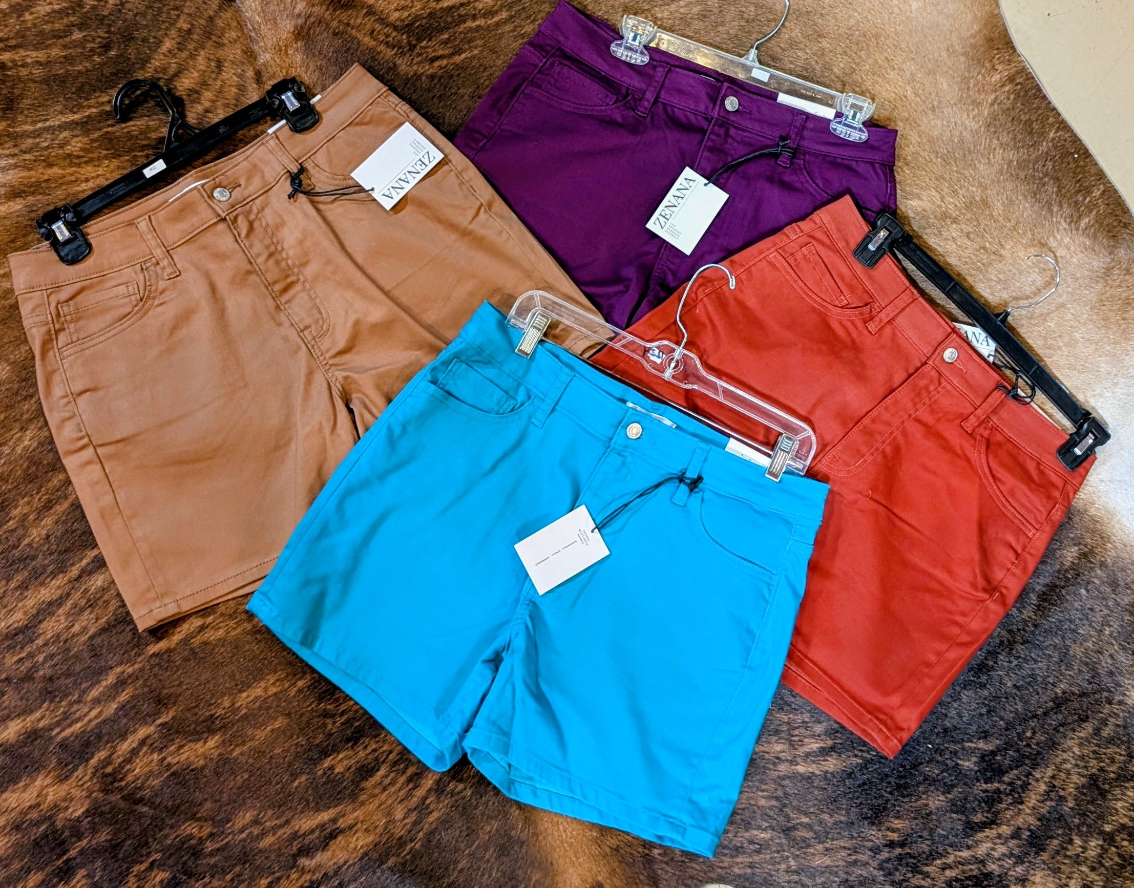 Four pairs of shorts in brown, purple, blue, and red on a wooden surface.