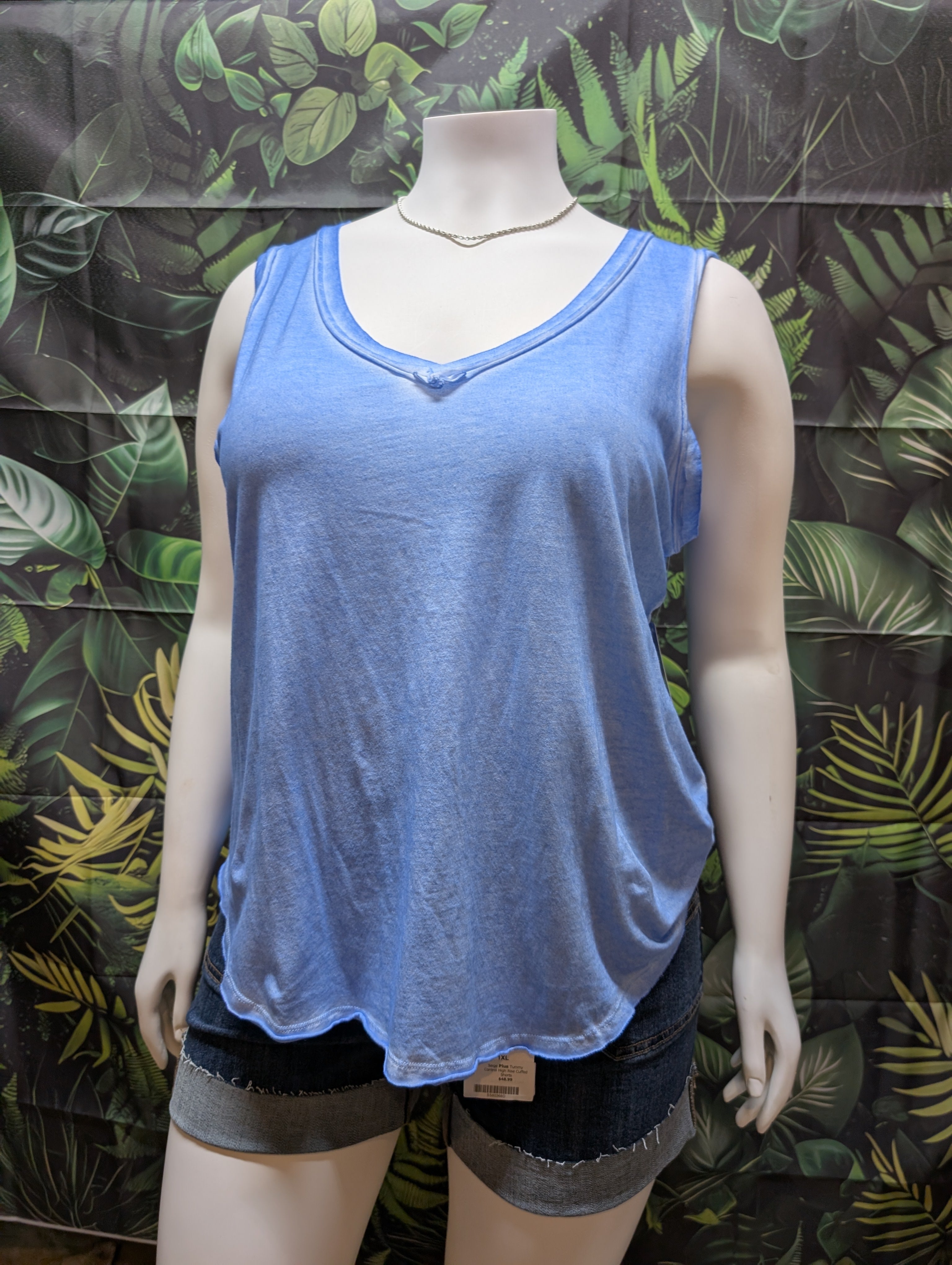 Mannequin wearing a blue tank top and black shorts against a leaf-patterned background